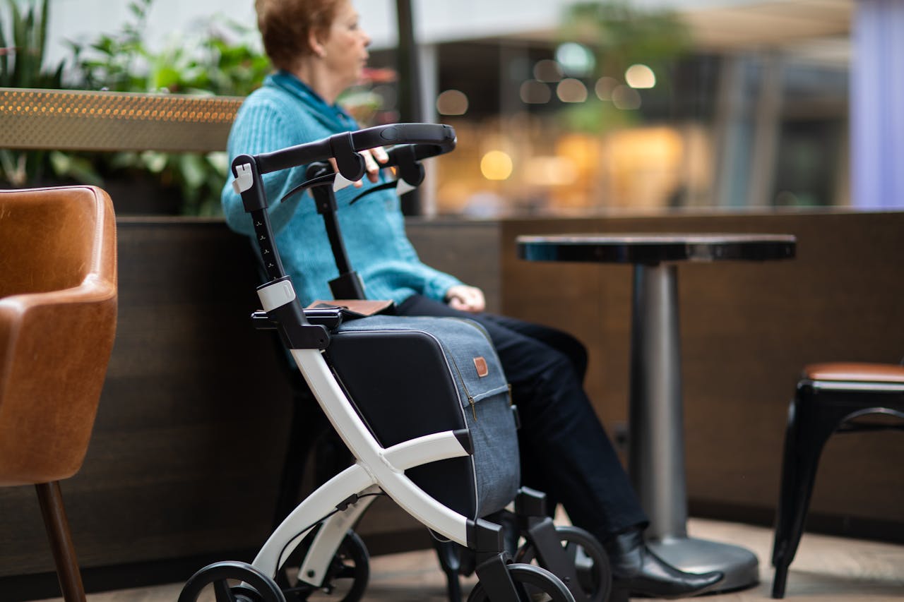 Elderly woman sits indoors in a mall with a rollator walker, enjoying leisure time.